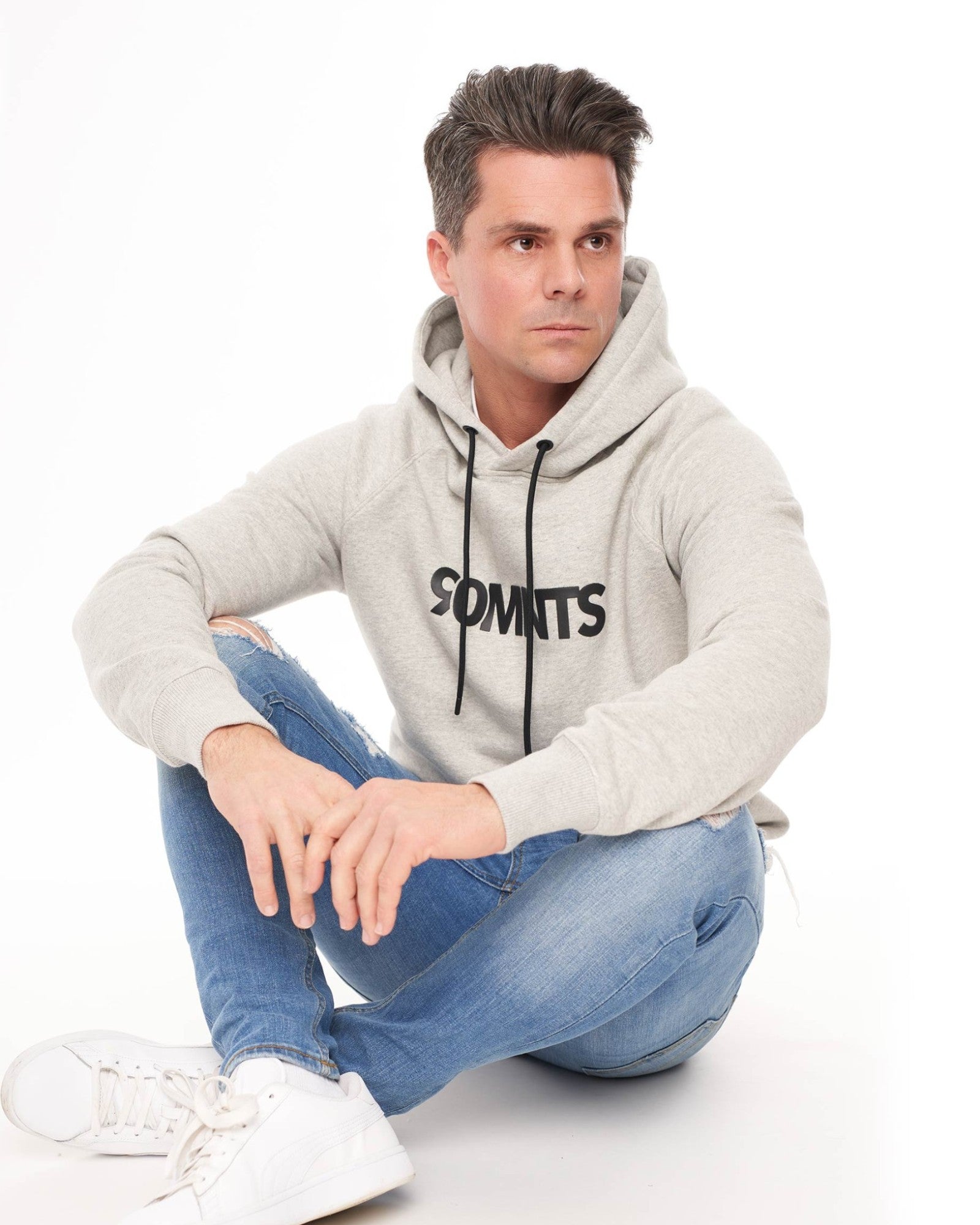 Männliches Model (sitzt) trägt den 90 Core Hoodie Grey