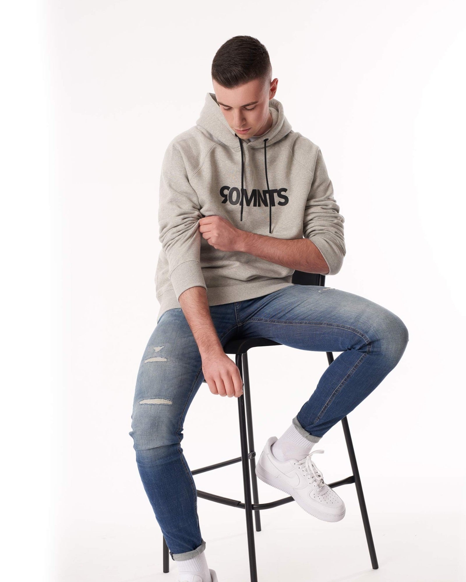 Männliches Model (sitzt auf einem Stuhl) trägt den 90 Core Hoodie Grey