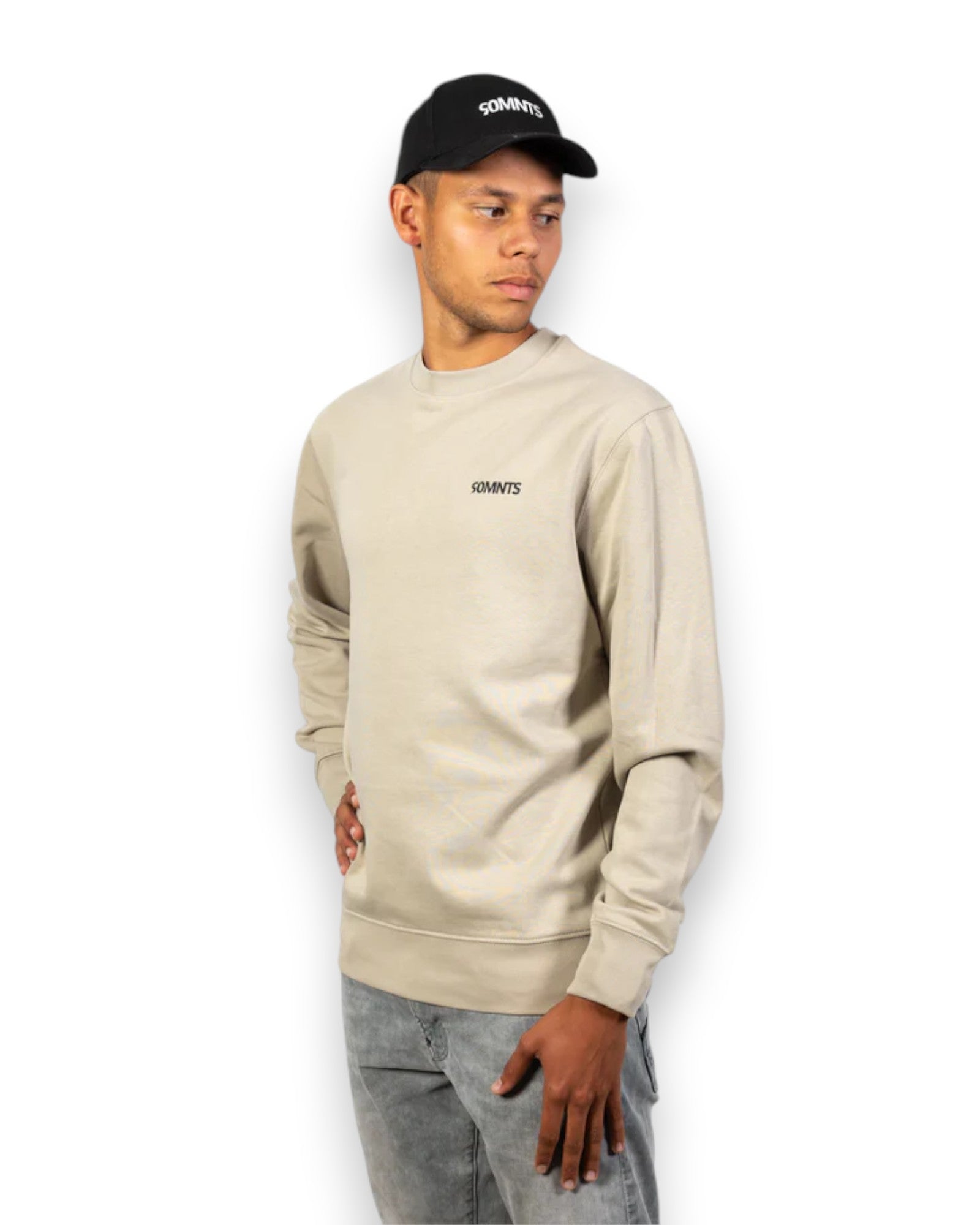 Männliches model mit 90MNTS Cap trägt Colours Sweater in Stone mit schwarzen Print